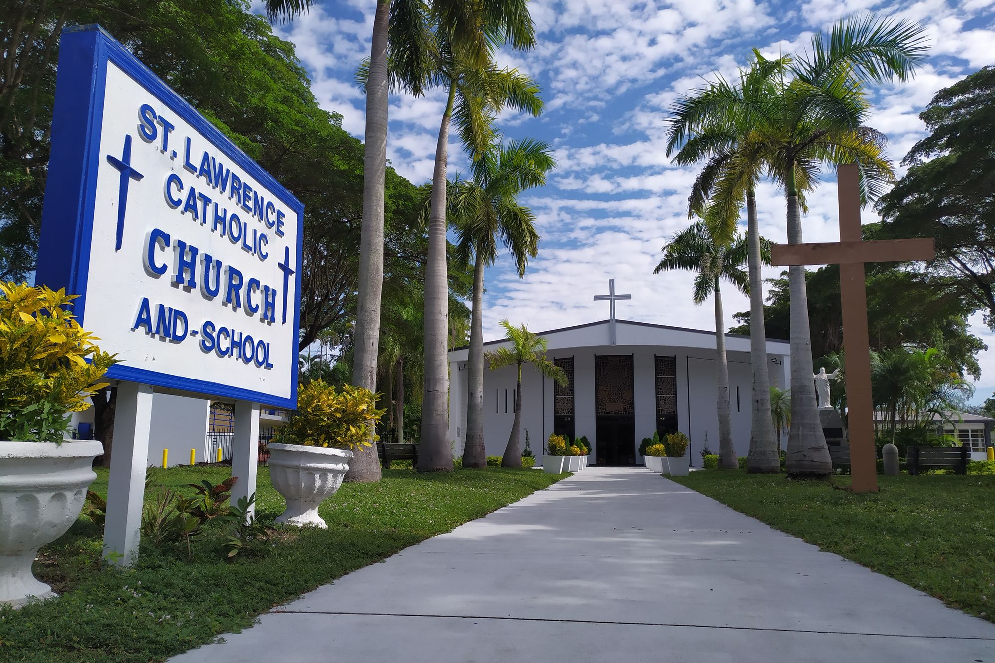 The entrance to St. Lawrence Catholic Church and School — the parish sign and cross beneath the royal palms